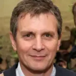 Illustrative portrait photo of a man with a soft smile wearing a dark jacket, a placeholder and not a customer